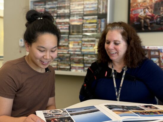 Claire Selinger, a University of Nebraska Omaha speech-language pathology student, sits with Andrea Fossum at QLI, reviewing a photo and memory book together during a weekly volunteer session.